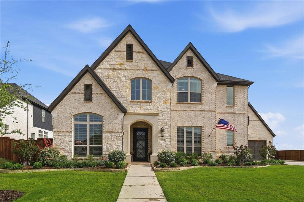 Stone veneer exterior with dark gabled rooflines, arched entry, and a prominent front door with decorative glass