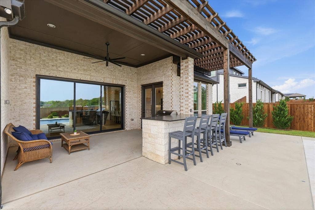 Covered patio featuring a built-in outdoor kitchen with bar seating, a pergola extension, and a ceiling fan