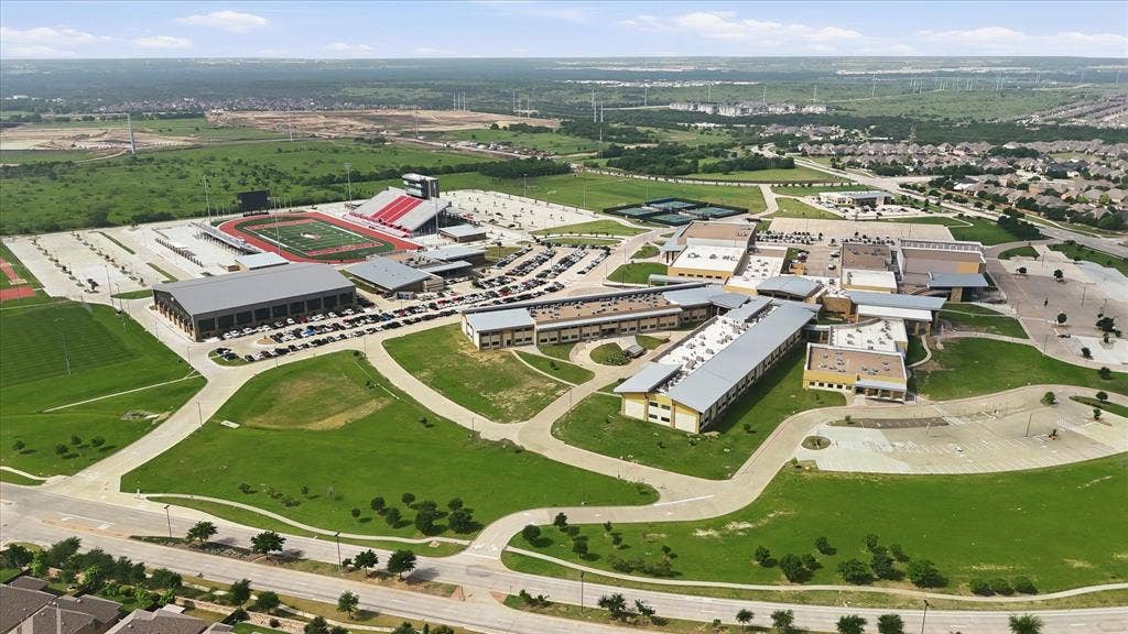 Expansive campus featuring multiple academic buildings, athletic fields, a stadium with red bleachers, and extensive parking areas
