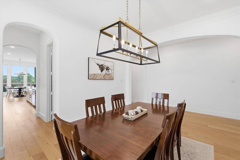 Dining area featuring a linear chandelier with a black and brass finish, white walls, and wood-finish flooring