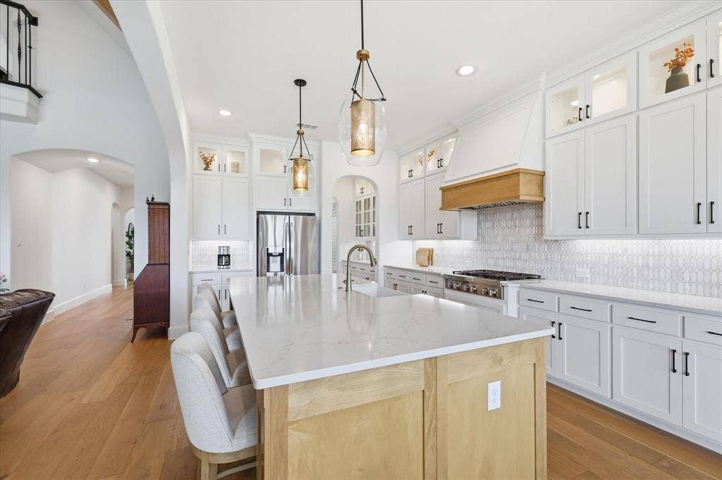 Gourmet kitchen featuring a large central island with seating, white shaker cabinetry, stainless steel appliances, a stylish tiled backsplash, and recessed and pendant lighting