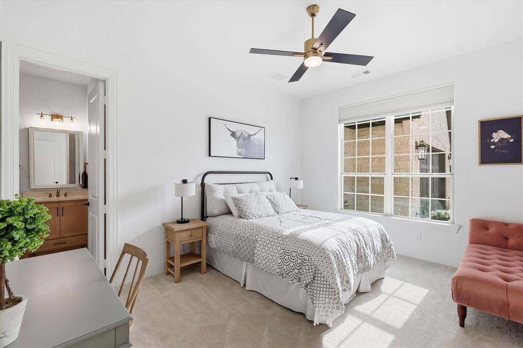 Well-lit interior room featuring a large window with white grilles, a ceiling fan with gold and black accents, and plush carpeting