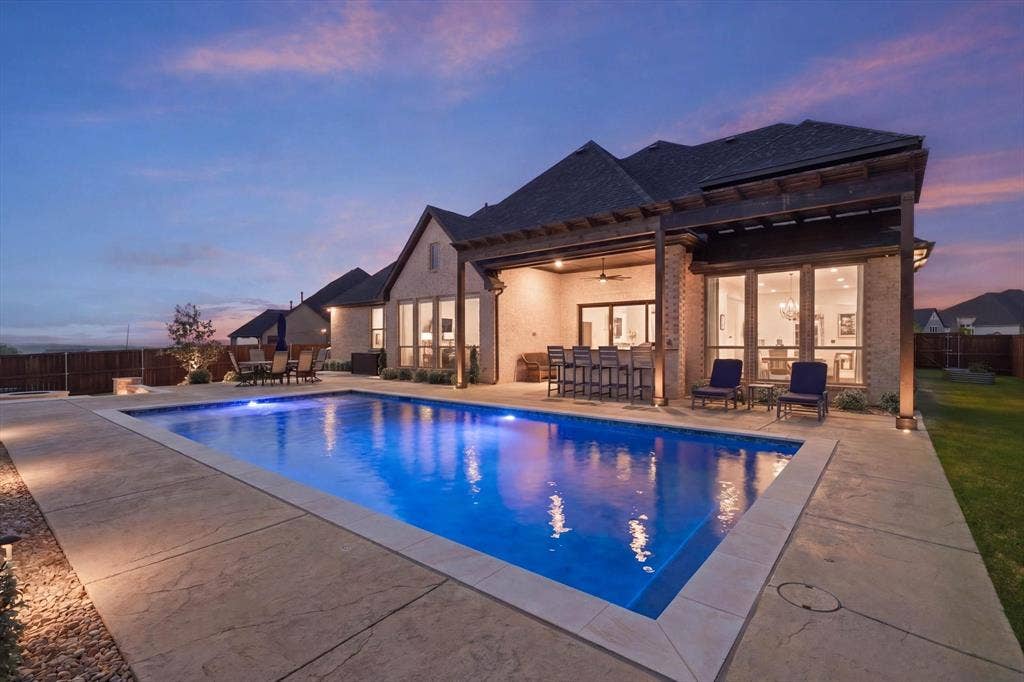 Backyard oasis featuring an illuminated swimming pool, stamped concrete patio, and a covered outdoor living area