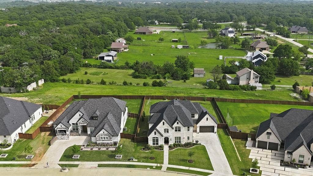 Aerial view of the Front exterior featuring a stone exterior, an attached 4-car garage, driveway, and a fenced backyard