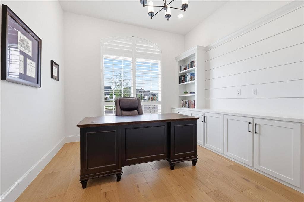 Arched window with plantation shutters, wood-finish flooring, built-in shelving, white cabinetry with matte black hardware, and shiplap wall detailing