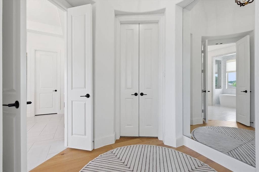 Hallway with light wood-finish flooring, white paneled doors with matte black hardware, and a full-length mirror