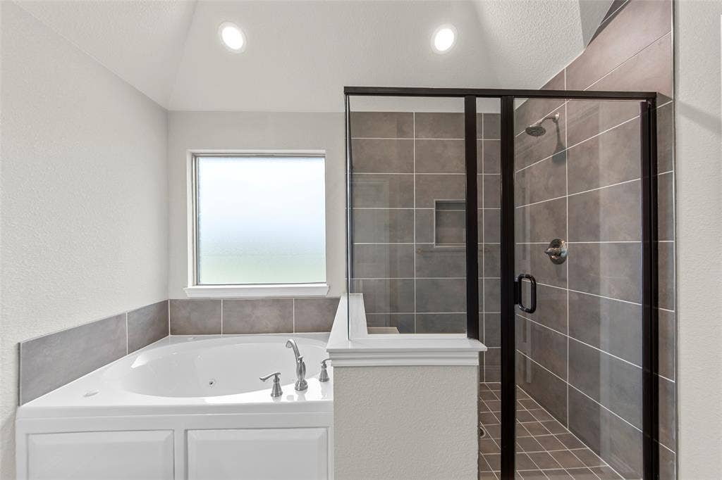 18310 CHIPPEWA Court, Terrell, TX 75160 Soaking tub with chrome fixtures, enclosed shower with dark-framed glass, recessed shower niche, and tiled walls