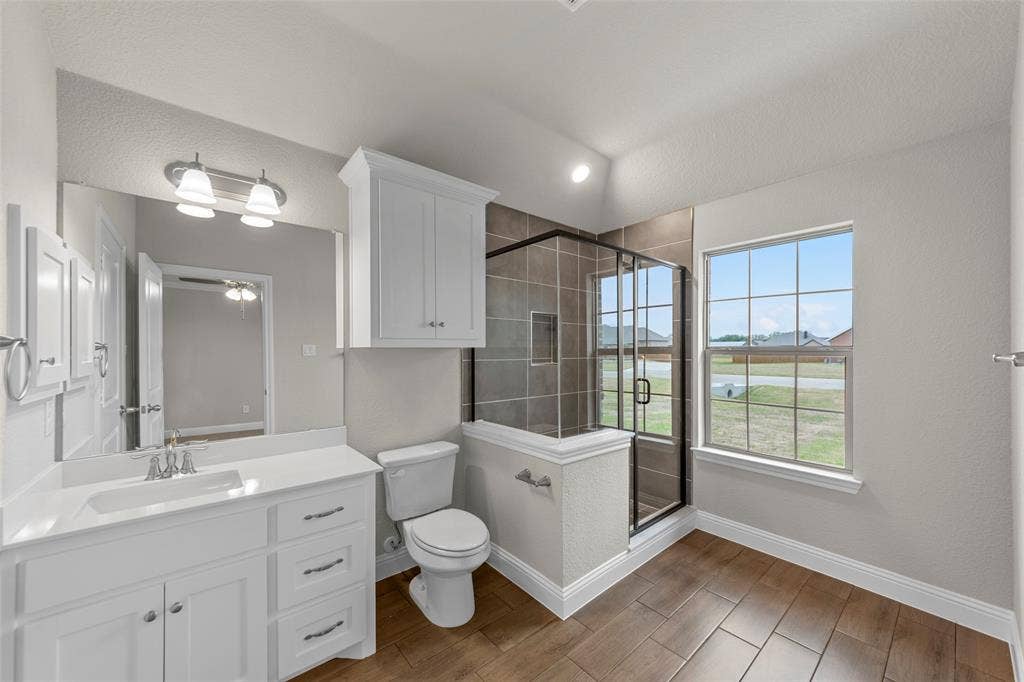 18310 CHIPPEWA Court, Terrell, TX 75160 Bathroom featuring a single vanity with white cabinetry, a walk-in shower with dark-toned tile surround, wood-finish flooring, a toilet, and an overhead storage cabinet