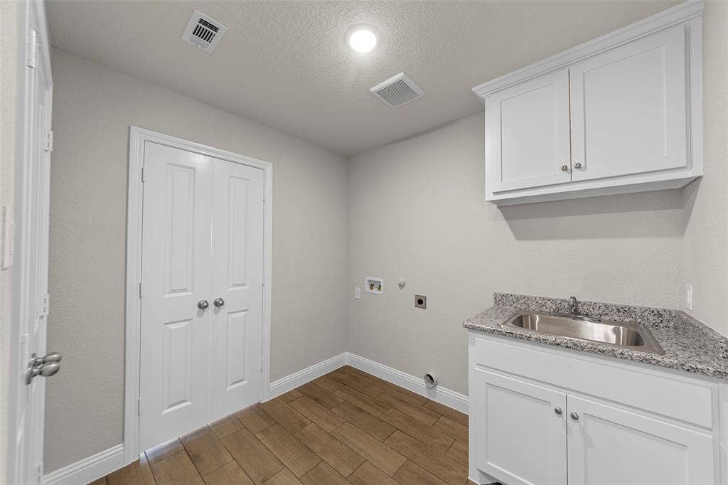 18310 CHIPPEWA Court, Terrell, TX 75160 Dedicated utility space featuring wood-finish flooring, white cabinetry, a stainless steel sink with a granite countertop, and bi-fold doors