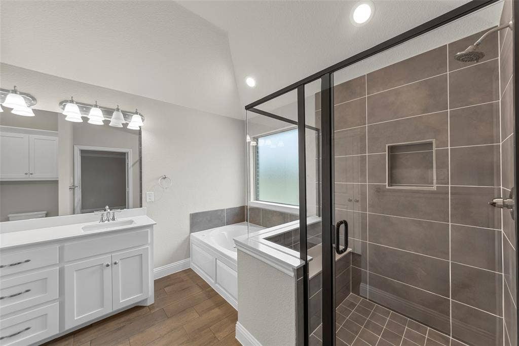 18310 CHIPPEWA Court, Terrell, TX 75160 Bathroom featuring a glass-enclosed shower with tiled walls and floor, a built-in shower niche, and a bathtub with a privacy window