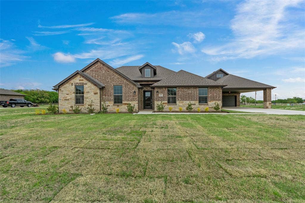 18310 CHIPPEWA Court, Terrell, TX 75160 Two-tone brick and stone exterior featuring an attached covered carport, dark shingle roofing, and a prominent front door