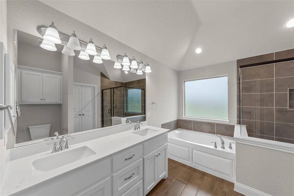 18310 CHIPPEWA Court, Terrell, TX 75160 Spacious bathroom featuring a dual vanity with white cabinetry and chrome fixtures, a large soaking tub, a tiled walk-in shower with a glass enclosure, and wood-finish flooring