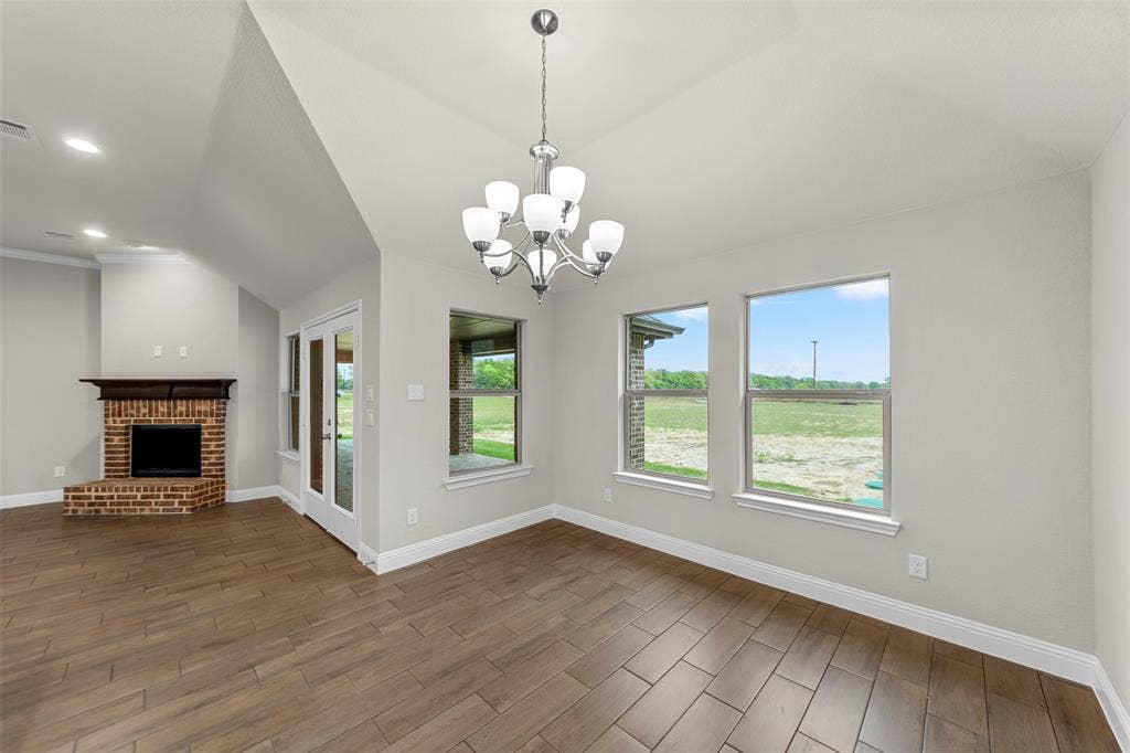 18310 CHIPPEWA Court, Terrell, TX 75160 Open concept living space featuring vaulted ceilings, wood-finish flooring, a brick-surround fireplace with a wood mantle, and a glass-paneled door