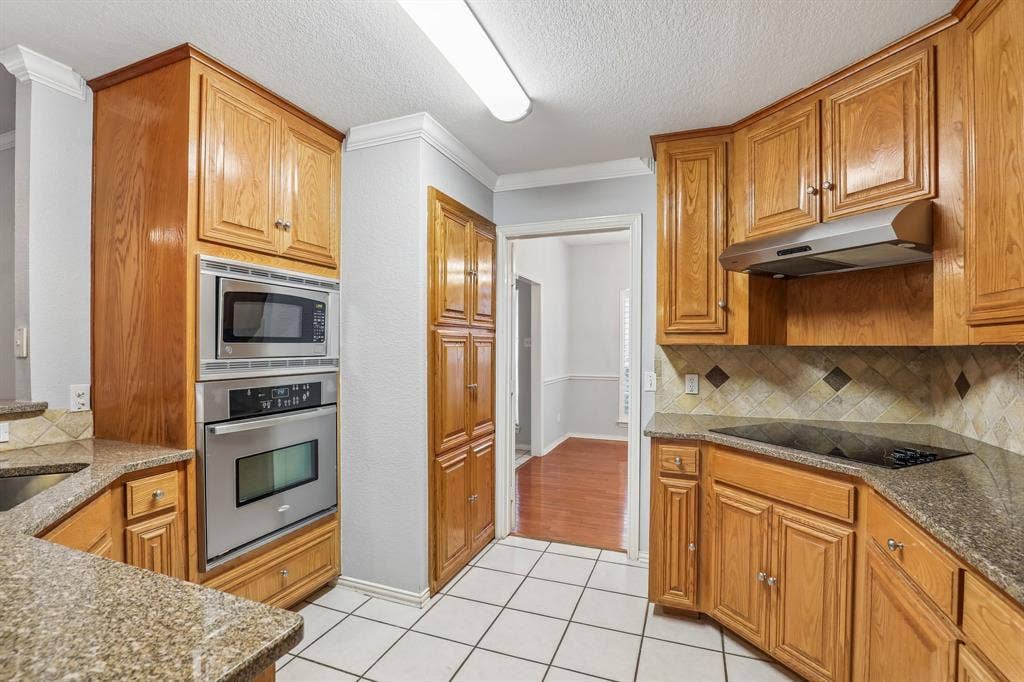 4124 Cory Lee Court, Arlington, TX 76015 Kitchen featuring wood cabinetry, stainless steel built-in microwave and oven, a black cooktop, tiled backsplash with decorative accents, and speckled countertops