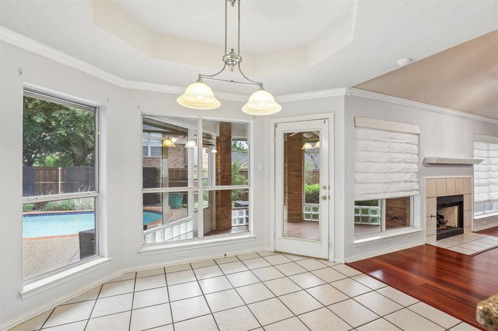 4124 Cory Lee Court, Arlington, TX 76015 Tiled flooring in a bright dining area with an overhead chandelier, featuring multiple windows overlooking a backyard pool, a glass-paneled door, and a fireplace with a tiled hearth