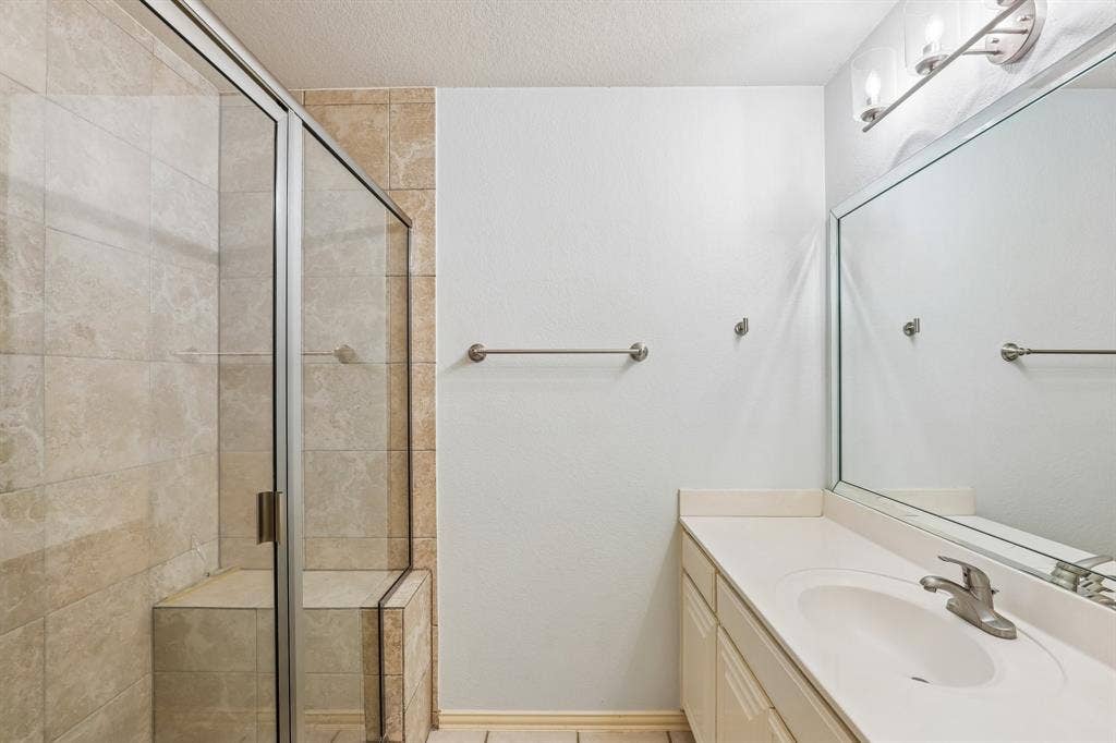4124 Cory Lee Court, Arlington, TX 76015 Bathroom featuring a glass-enclosed shower with a built-in bench and large format wall tiles, vanity with an integrated sink, and a large mirror with overhead lighting