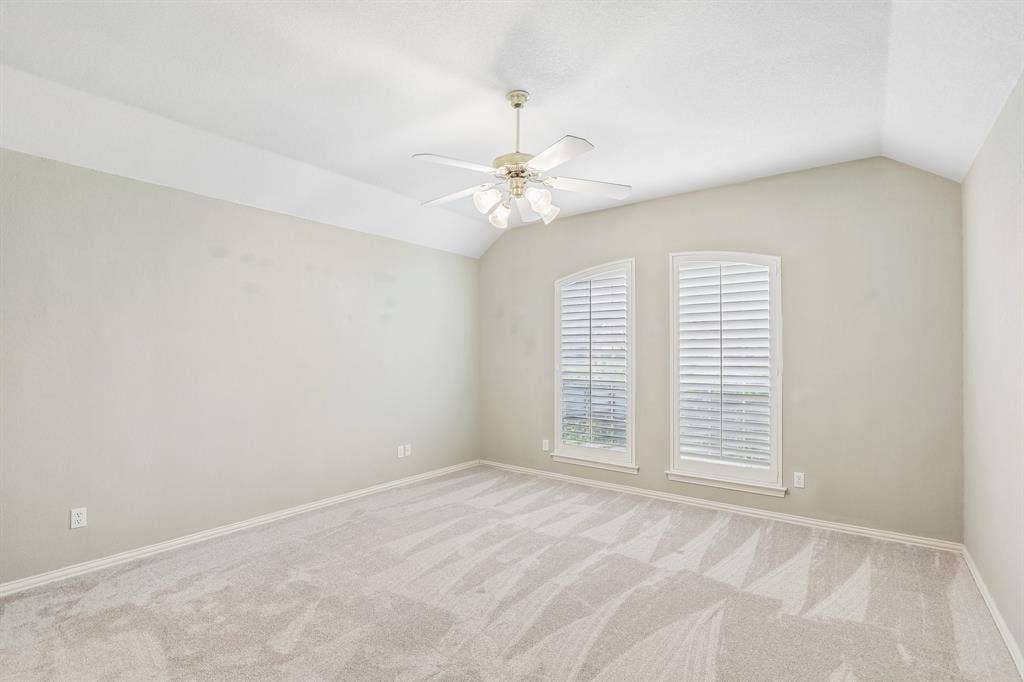4124 Cory Lee Court, Arlington, TX 76015 Spacious room featuring vaulted ceilings, a ceiling fan, two arched windows with louvered shutters, and light-toned carpet flooring