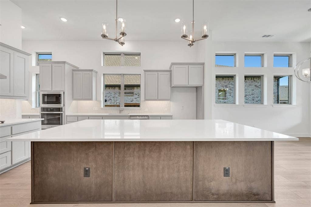 1611 Cedarberry Drive, Northlake, TX 76226 Kitchen featuring a large central island with a light-toned countertop, light gray cabinetry, built-in stainless steel appliances, and multiple windows providing ample natural light
