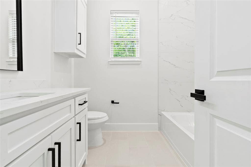 Bathroom featuring a white vanity with quartz countertop, integrated sink, and black hardware