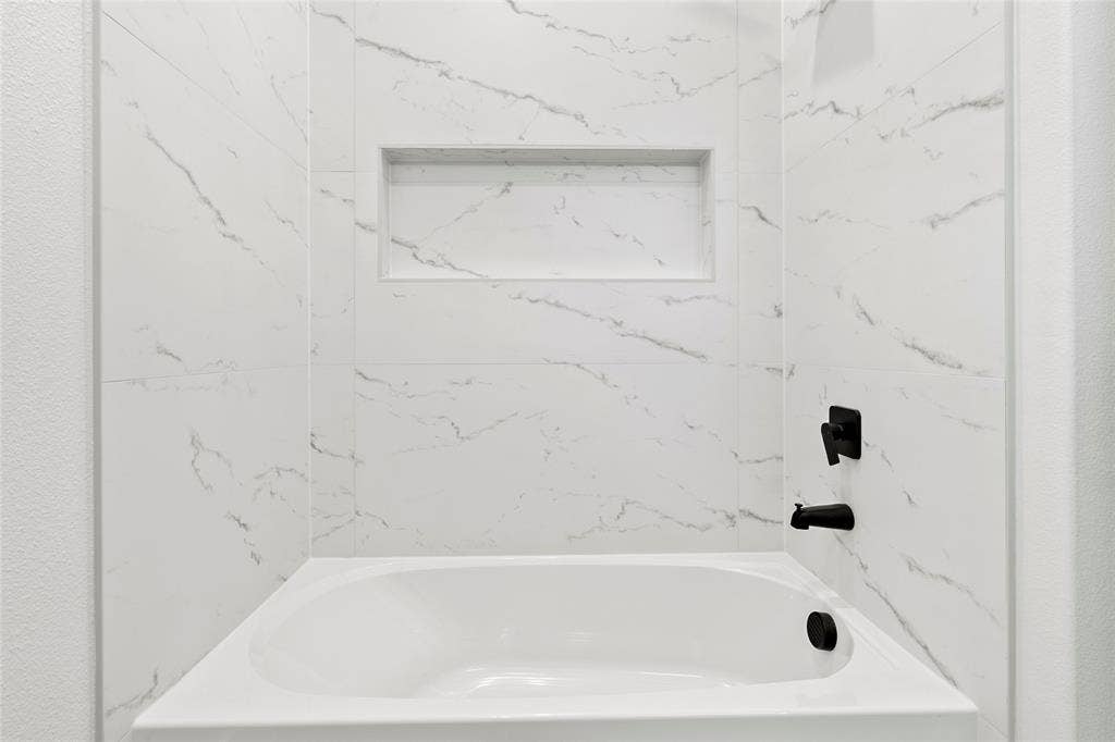 Bathtub with surrounding marble-patterned wall tile, featuring a recessed niche and matte black fixtures