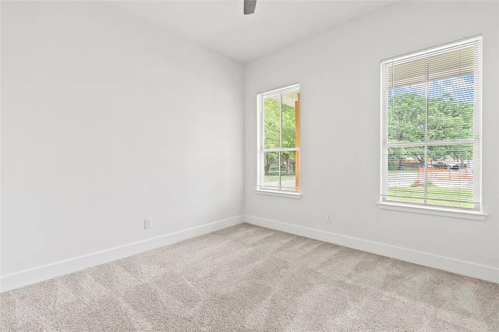 Carpeted room featuring two windows with horizontal blinds, white walls, and a ceiling fan