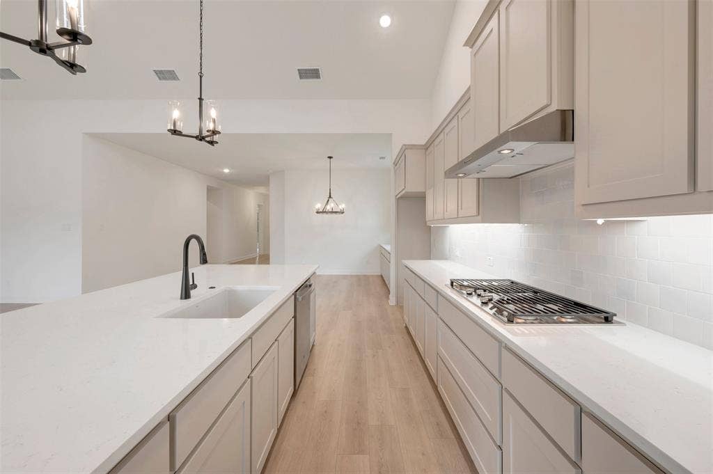 1605 Cedarberry Drive, Northlake, TX 76226 Expansive kitchen with an integrated gas cooktop, undercabinet lighting, wood-finish flooring, and a large central island with an undermount sink
