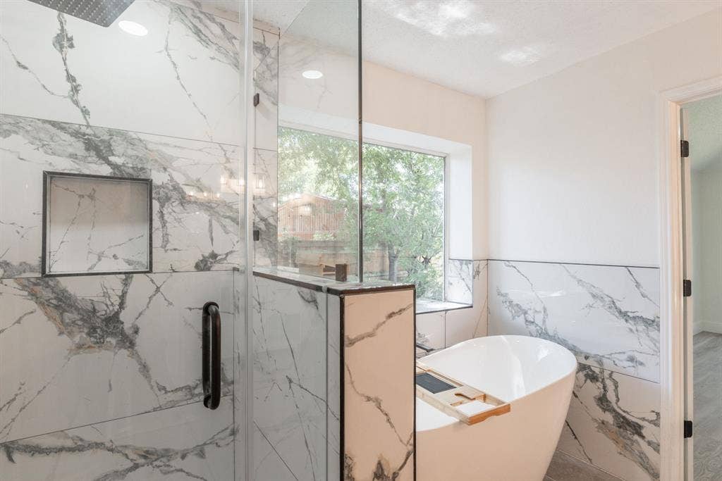 Bathroom featuring a freestanding soaking tub, a walk-in shower with clear glass enclosure and black hardware, and large format marble-look tile