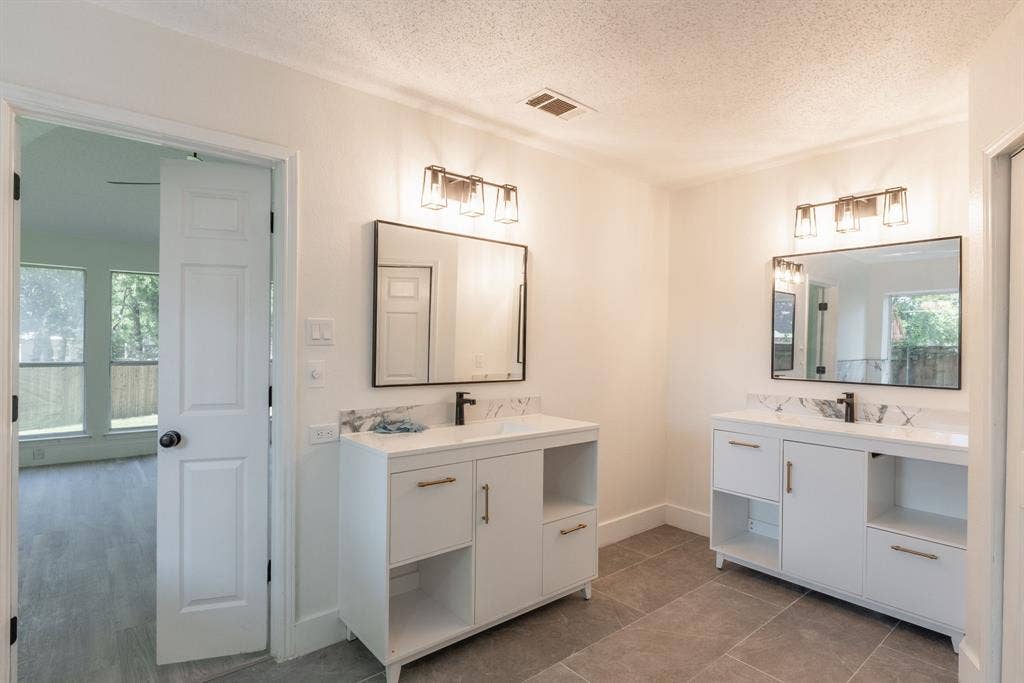 Double vanity bathroom featuring white cabinetry, integrated sinks, dark bronze hardware, and large format floor tiling