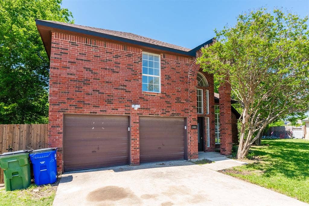 Brick exterior featuring a two-car garage, concrete driveway, and established landscaping
