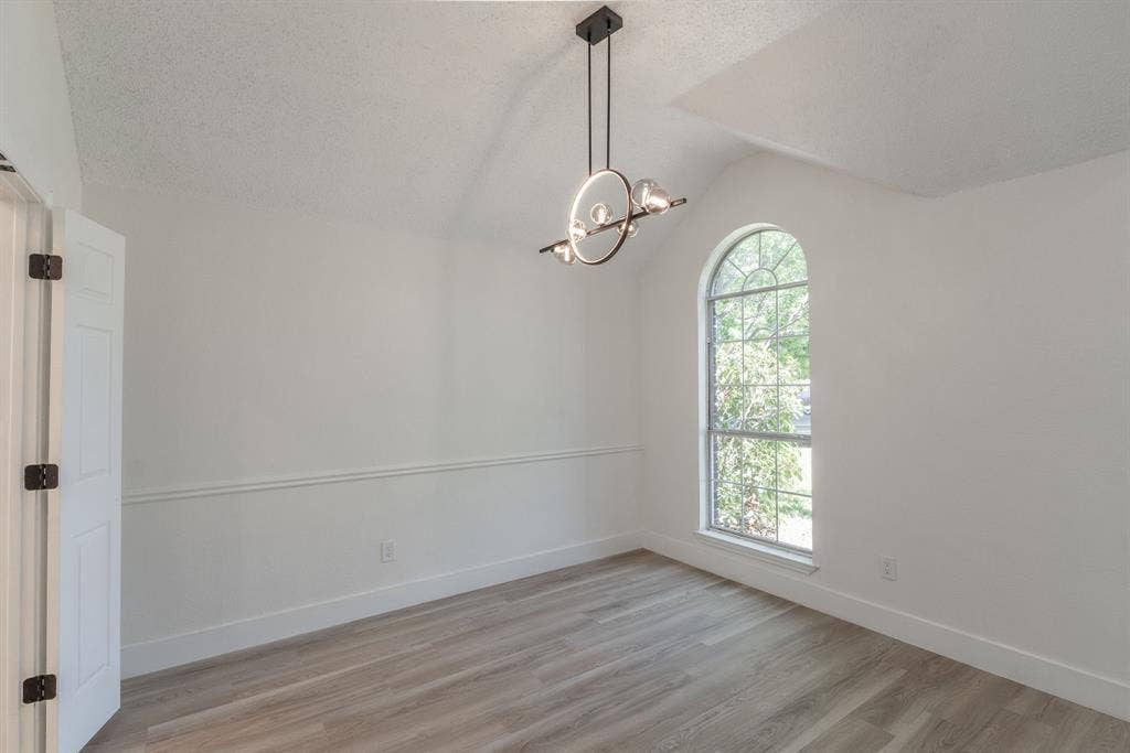Interior space featuring an arched window, wood-finish flooring, a modern chandelier, vaulted ceiling, and chair rail molding