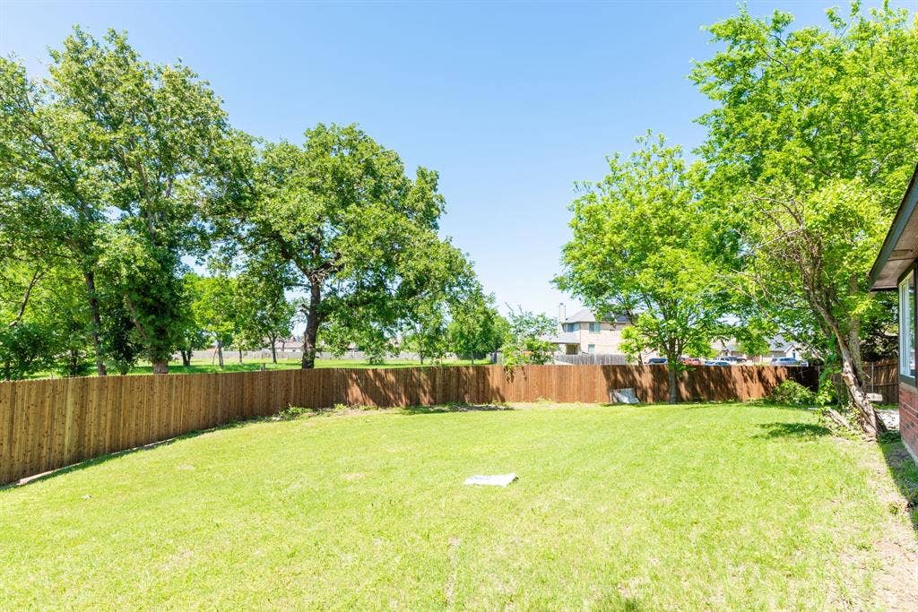 Spacious backyard featuring a privacy fence, mature trees, and a verdant lawn
