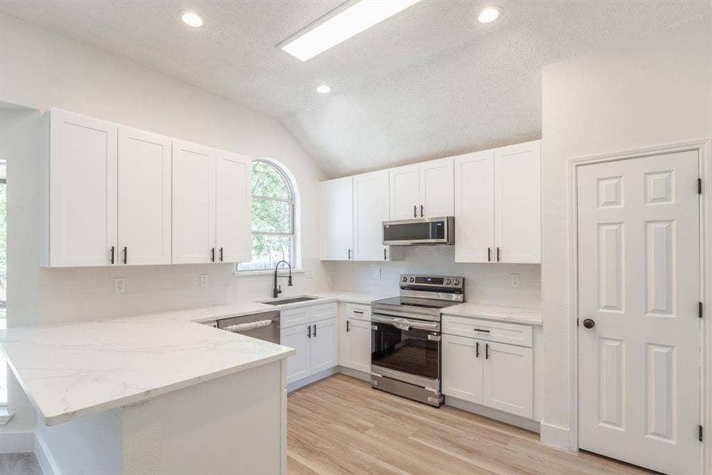 Modern kitchen featuring white shaker cabinetry, stainless steel appliances, marble-look countertops, and wood-finish flooring