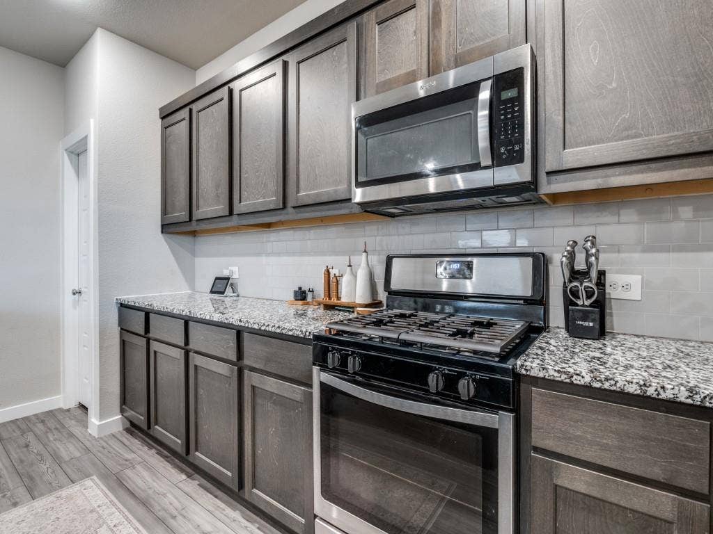626 Congressional Avenue, Red Oak, TX 75154 Kitchen featuring wood-finish cabinetry, granite-style countertops, stainless steel appliances, a gas range, and a subway tile backsplash