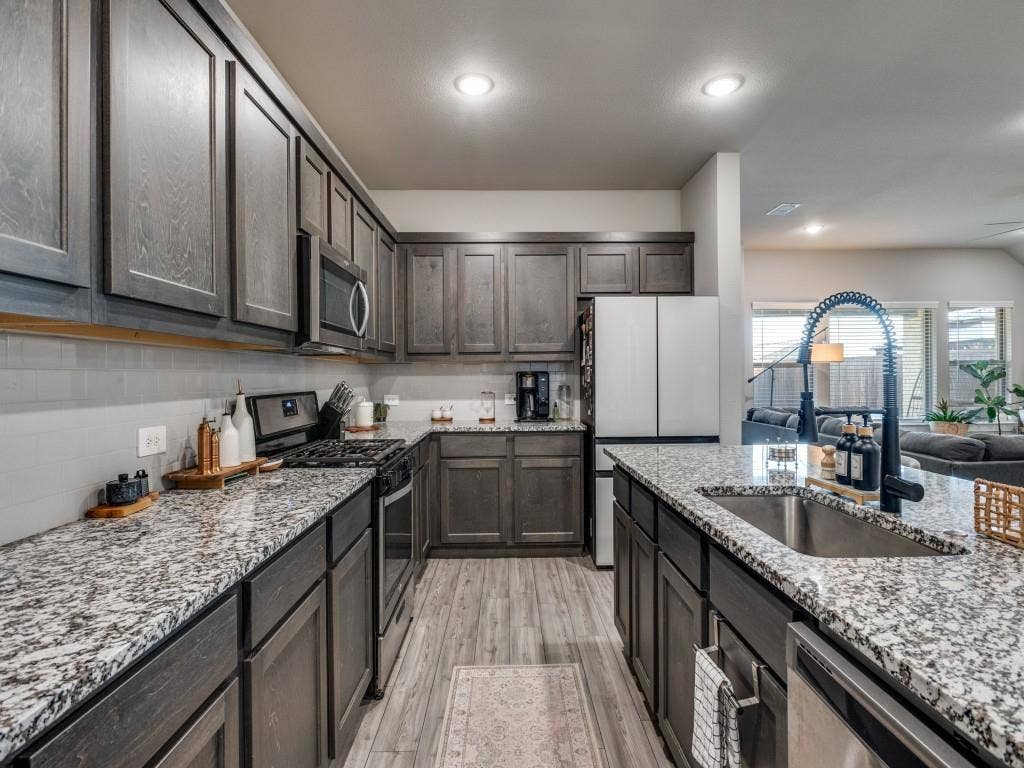 626 Congressional Avenue, Red Oak, TX 75154 Contemporary kitchen featuring dark wood-finish cabinetry, speckled countertops, stainless steel appliances, a tile backsplash, and wood-finish flooring