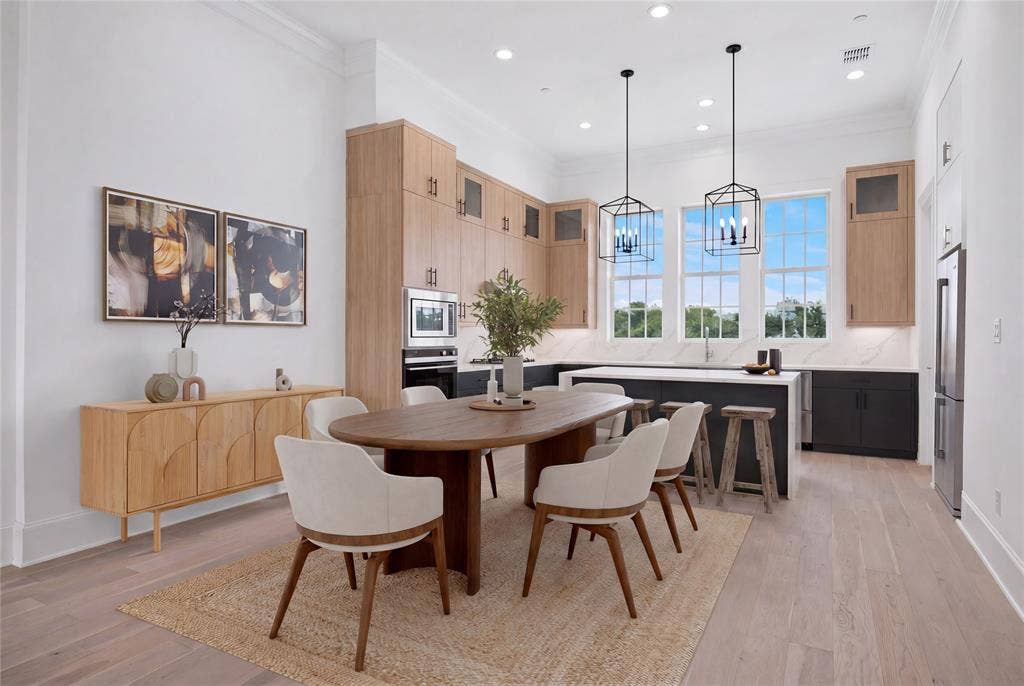 14956 Oak Street, Addison, TX 75001 Open-concept kitchen and dining area featuring light wood-finish flooring, a kitchen island with seating, stainless steel appliances, and abundant natural light from multiple large windows