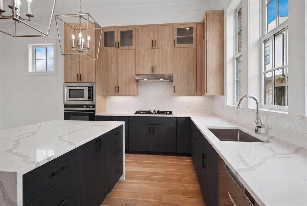 14956 Oak Street, Addison, TX 75001 Modern kitchen featuring light wood-finish upper cabinetry, dark lower cabinetry, and a large central island