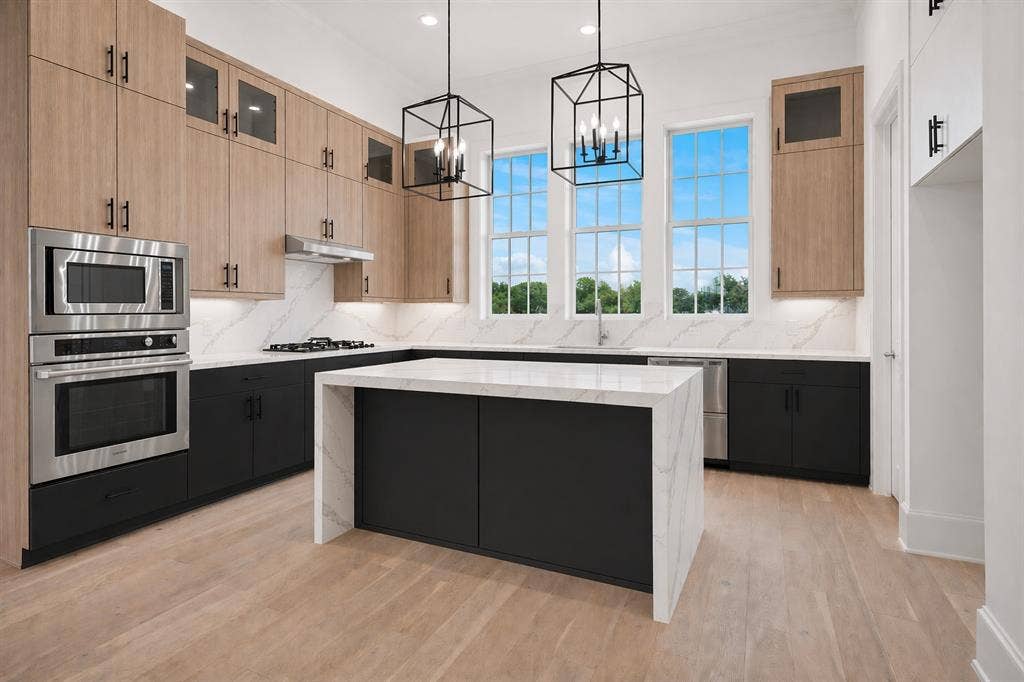 14956 Oak Street, Addison, TX 75001 Contemporary kitchen featuring a waterfall island with a stone countertop, light wood-finish flooring, and a suite of stainless steel appliances