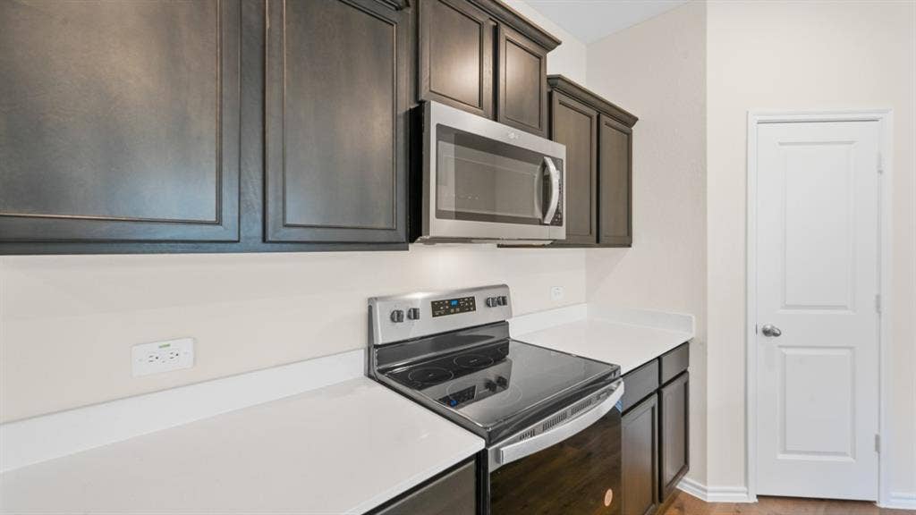 1647 Blaire Drive, Tyler, TX 75702 Kitchen featuring dark wood cabinetry, white countertops, stainless steel microwave, electric range, and a two-panel interior door
