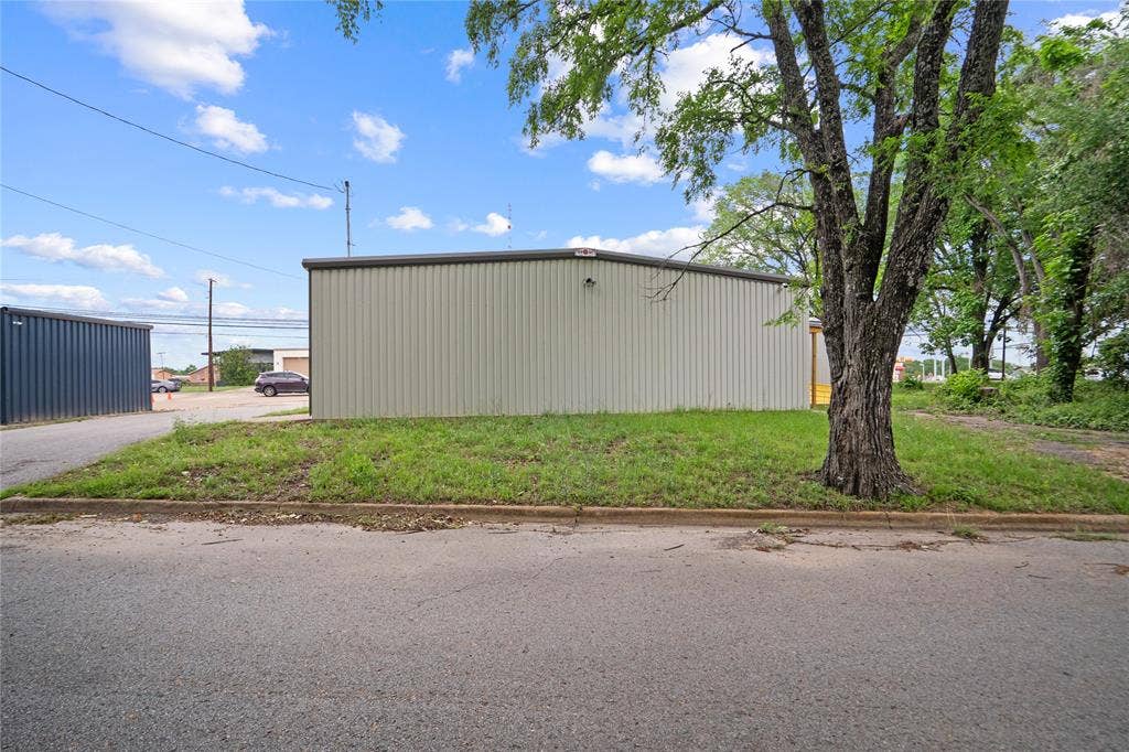 807 W Corsicana Street, Athens, TX 75751 Light-colored corrugated metal building with a dark gray trim, situated on a grassy lot