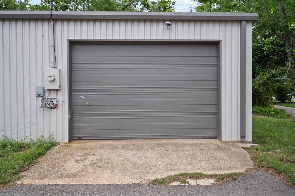 807 W Corsicana Street, Athens, TX 75751 Metal-sided building featuring a gray roll-up door, exterior electrical meter, and concrete approach pad