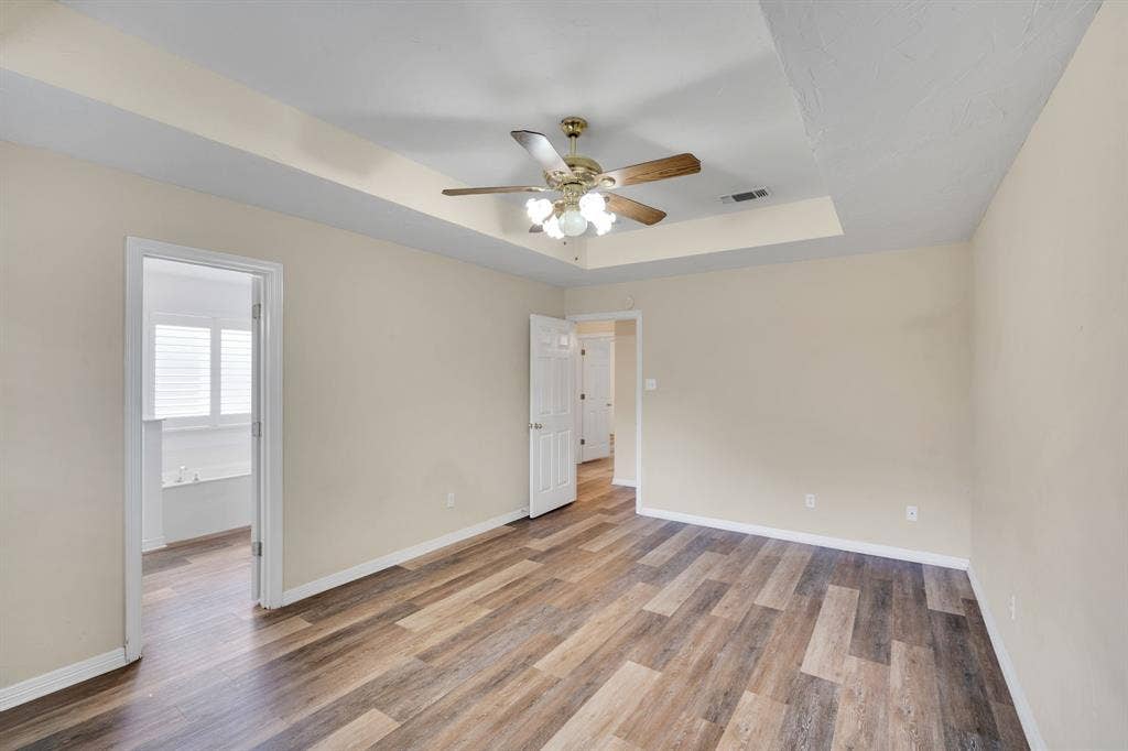 506 Whitney Drive, Midlothian, TX 76065 Spacious Primary room featuring wood-finish flooring, a tray ceiling, and a ceiling fan with integrated lighting