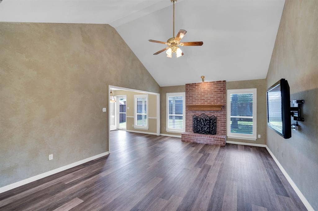506 Whitney Drive, Midlothian, TX 76065 Spacious living area featuring vaulted ceilings, wood-finish flooring, a brick fireplace with a wood mantle, and multiple windows with plantation shutters