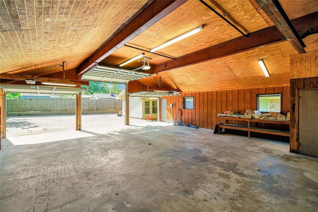 1114 Brookshire Drive, Tyler, TX 75071 Spacious multi-bay garage featuring a concrete floor, wood-paneled walls, and exposed beam ceiling