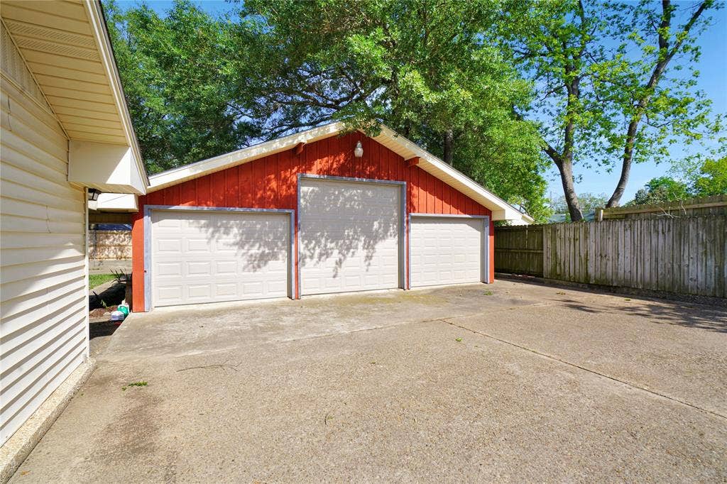 1114 Brookshire Drive, Tyler, TX 75071 Three-car garage with red siding, white garage doors, and a concrete driveway