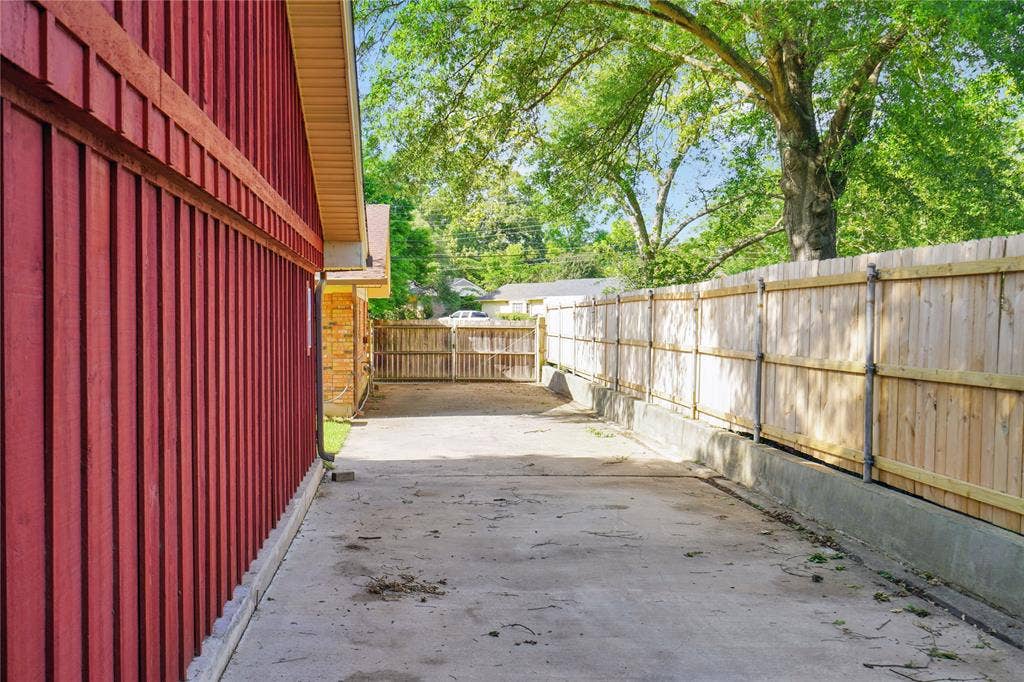 1114 Brookshire Drive, Tyler, TX 75071 Paved side yard featuring a red vertical siding exterior, a light wood-tone fence with metal posts, and a wood gate