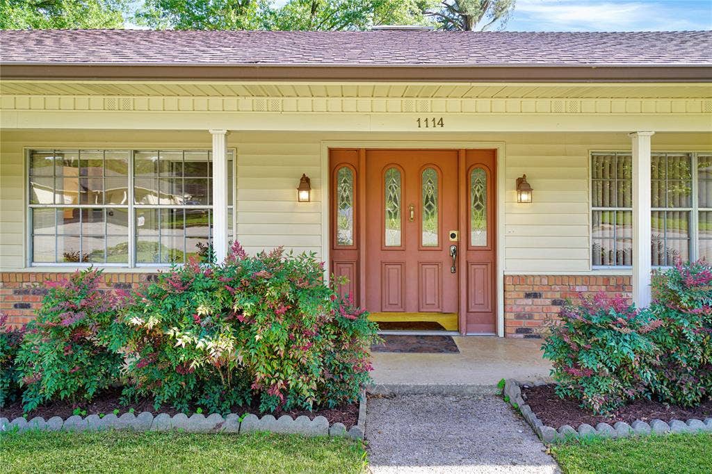 1114 Brookshire Drive, Tyler, TX 75071 Inviting front exterior featuring a covered porch, a three-panel entry door with decorative glass inserts, and brick accents
