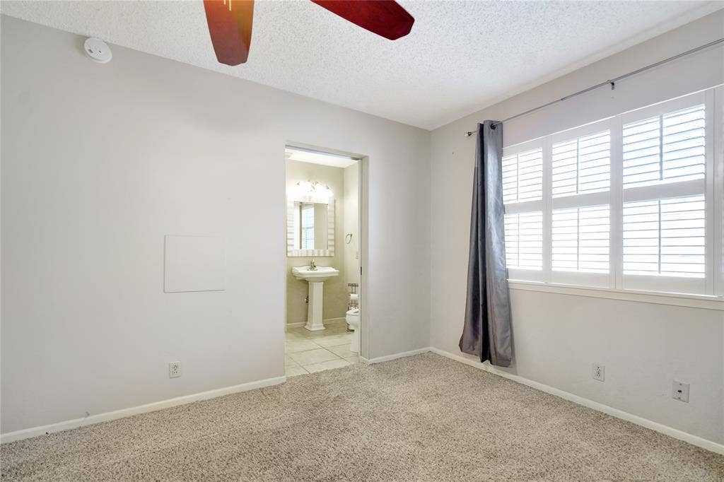 1114 Brookshire Drive, Tyler, TX 75071 Plush carpeted room featuring a ceiling fan, white plantation shutters, and an attached bathroom with a pedestal sink and tile flooring