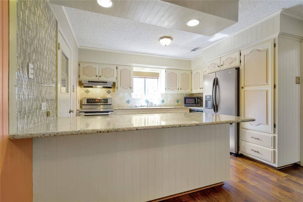 1114 Brookshire Drive, Tyler, TX 75071 Kitchen featuring an island with a light-toned countertop, white cabinetry, a tiled backsplash, and wood-finish flooring