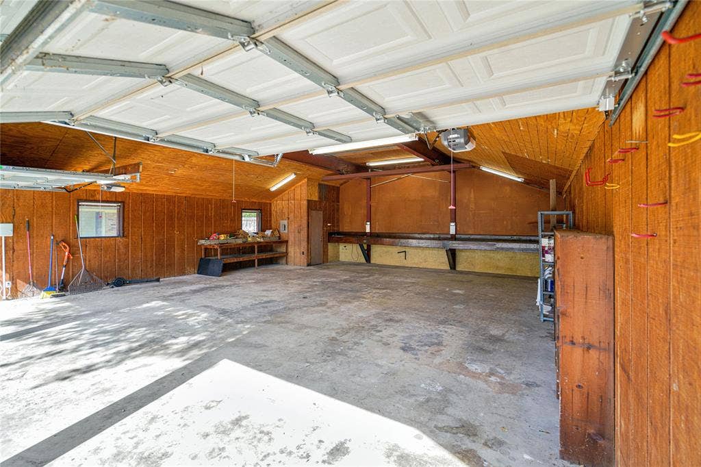 1114 Brookshire Drive, Tyler, TX 75071 Spacious garage featuring a concrete floor, wood panel walls, and an overhead garage door with track lighting