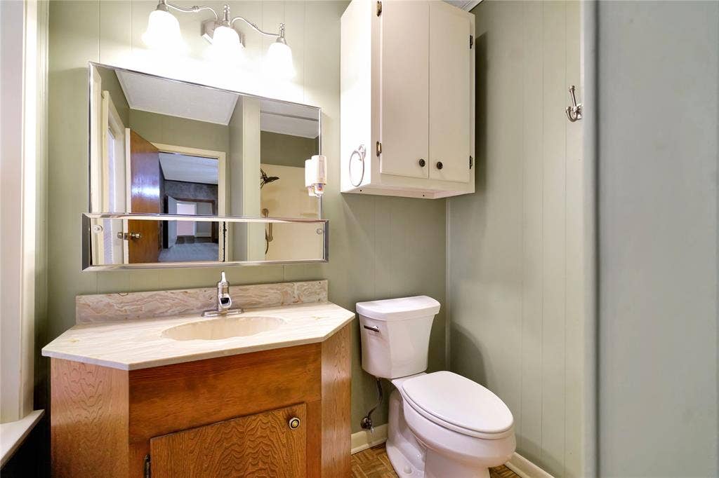 1114 Brookshire Drive, Tyler, TX 75071 Bathroom featuring a wood vanity with an integrated sink, a light-toned countertop, a tri-fold medicine cabinet, a wall-mounted light fixture, and vertical paneling